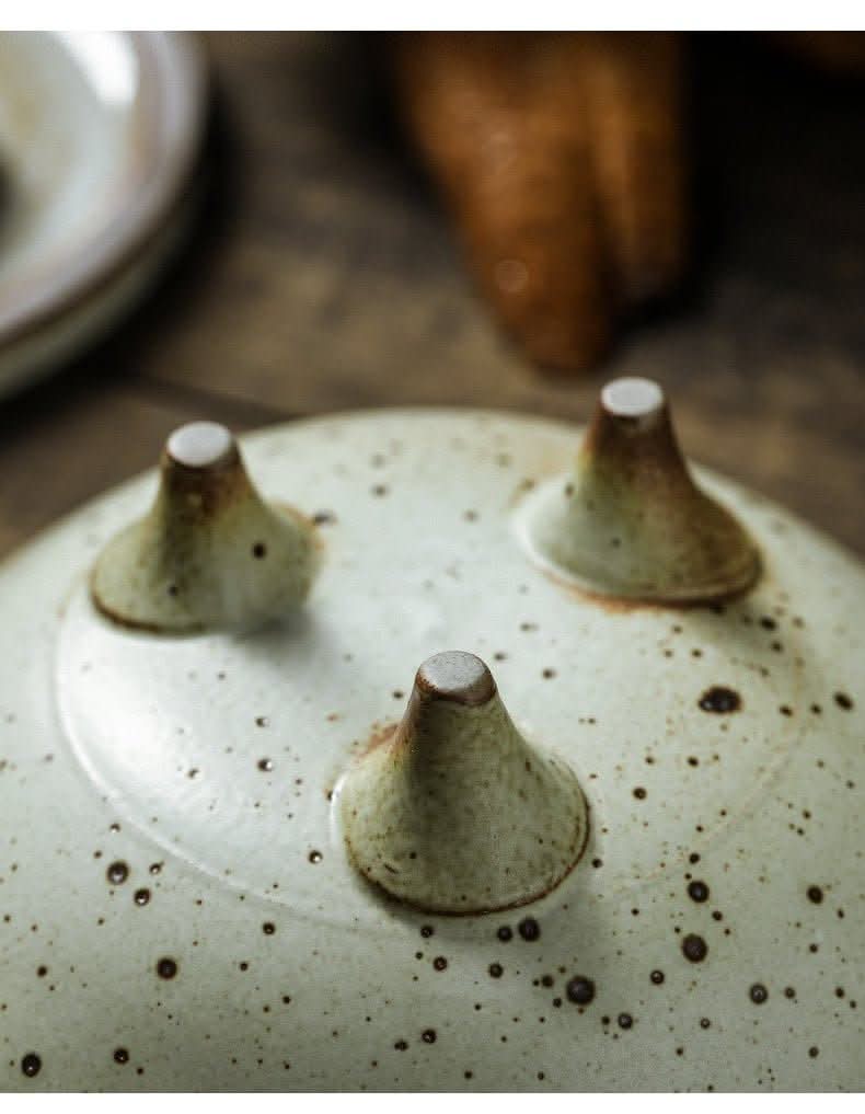 Close-up of a speckled ceramic Tripod Stoneware Fruit Plate with three conical feet.