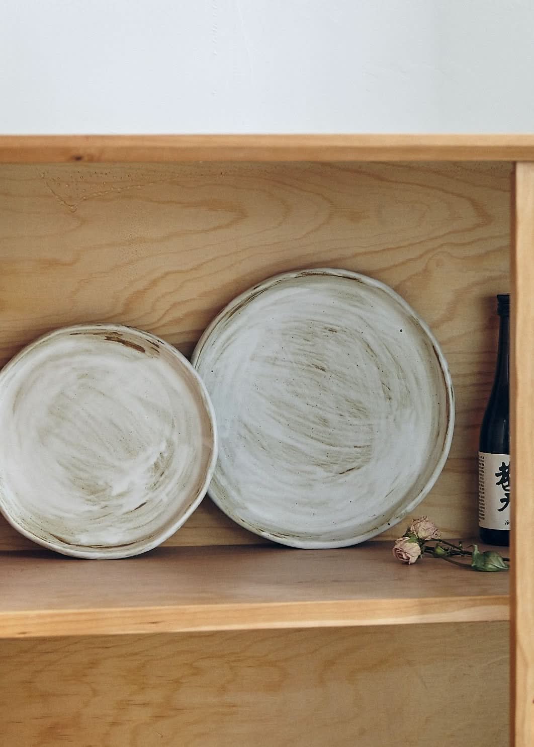 Two Stoneware Plates With White Glaze, with rustic texture, on a wooden shelf.