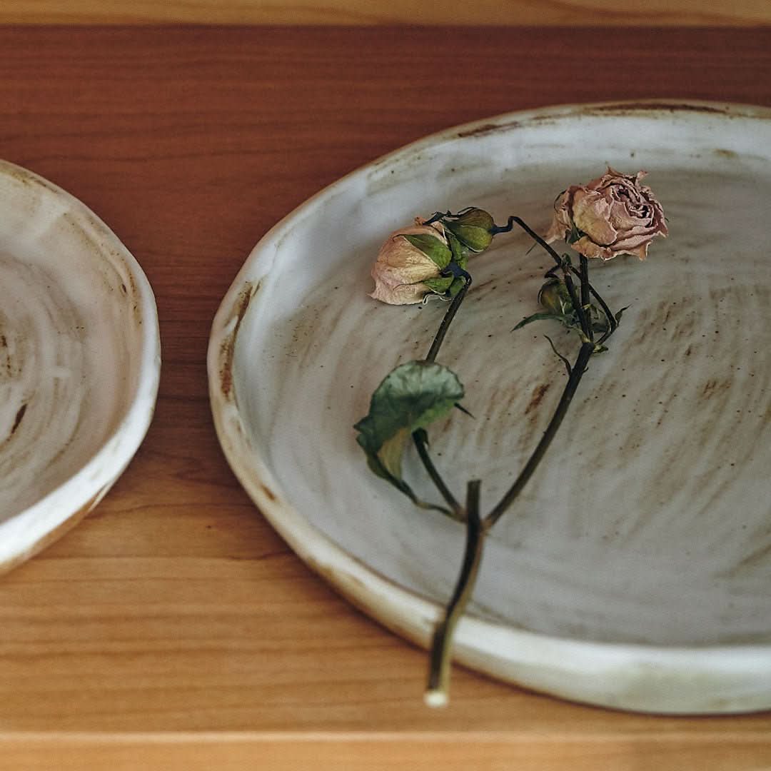 Stoneware plates with white glaze and dried roses on a wooden surface.