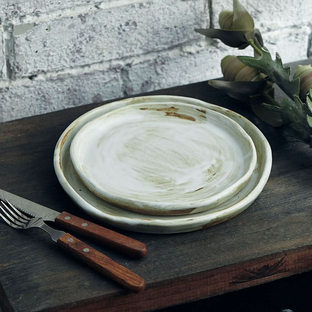 Two stoneware plates with white glaze, rustic, on a wooden surface with fork.