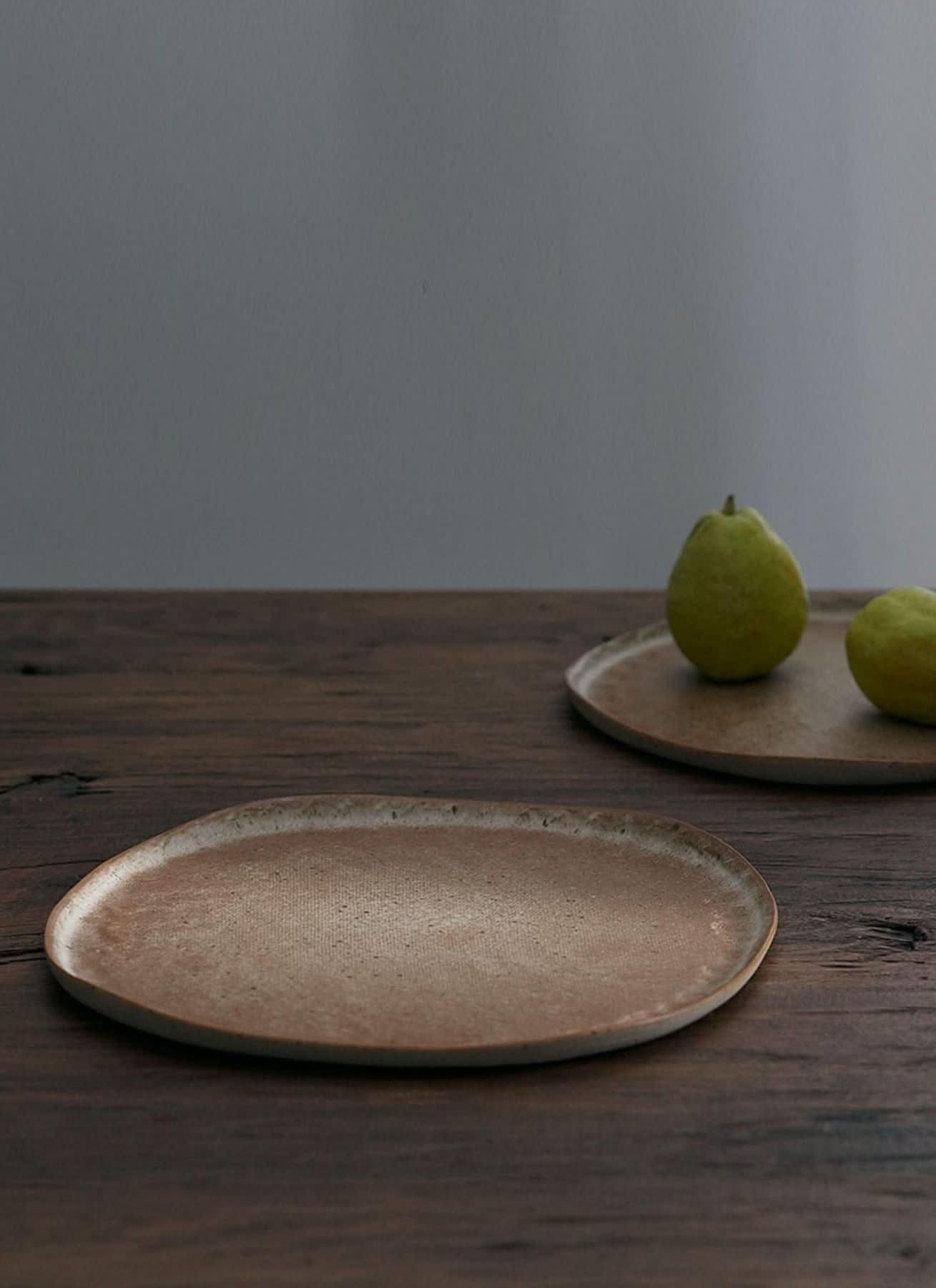 Unglazed large irregular coarse pottery flat plate on rustic wood table, home decor.