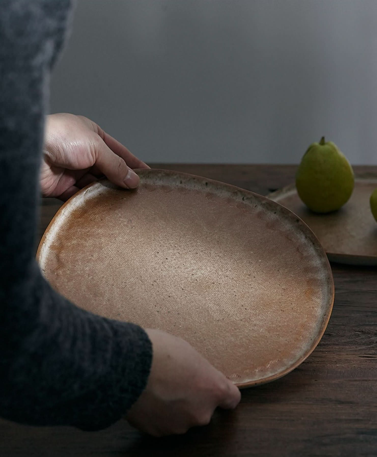 Unglazed large irregular coarse pottery flat plate in natural earthy tones on a wooden table.