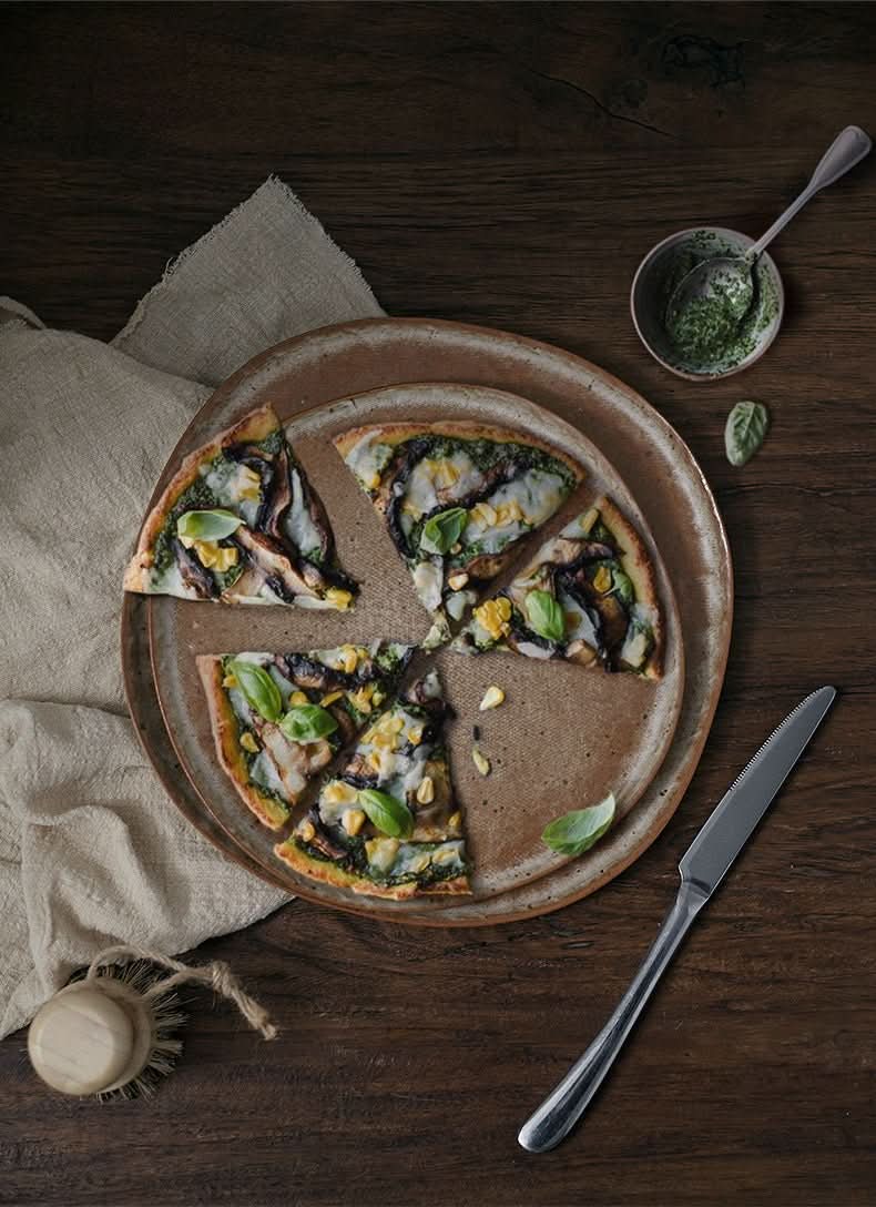 Unglazed large irregular coarse pottery flat plate with pizza, rustic home decor setting.