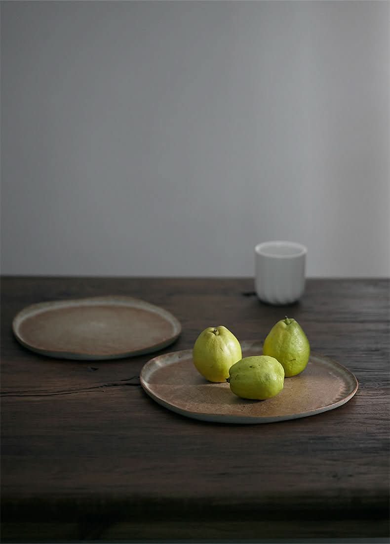 Unglazed large irregular coarse pottery flat plate on wooden table with guavas.