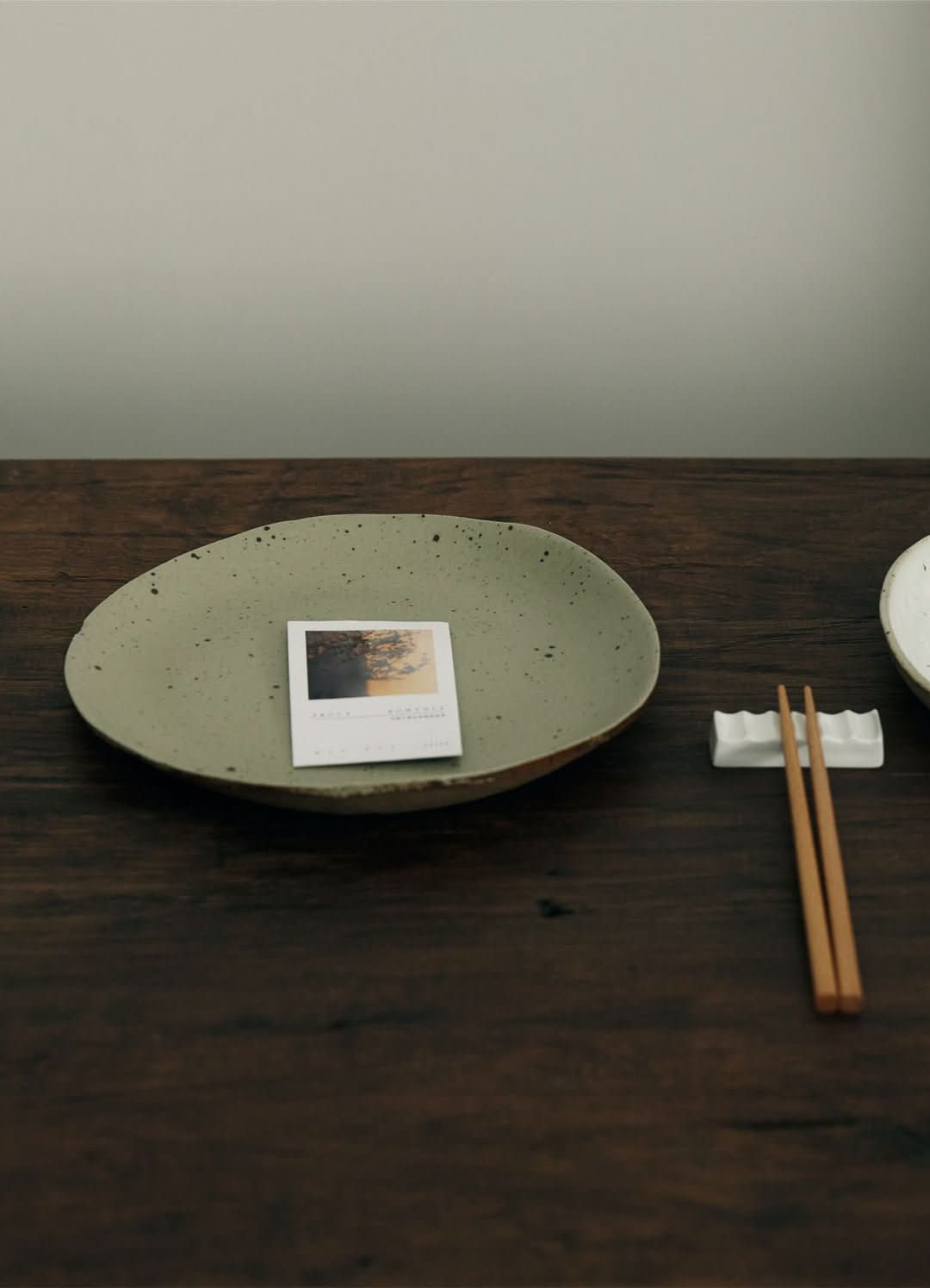 Light green handmade unglazed earthenware dinner plate with speckled finish, on a dark wooden table.