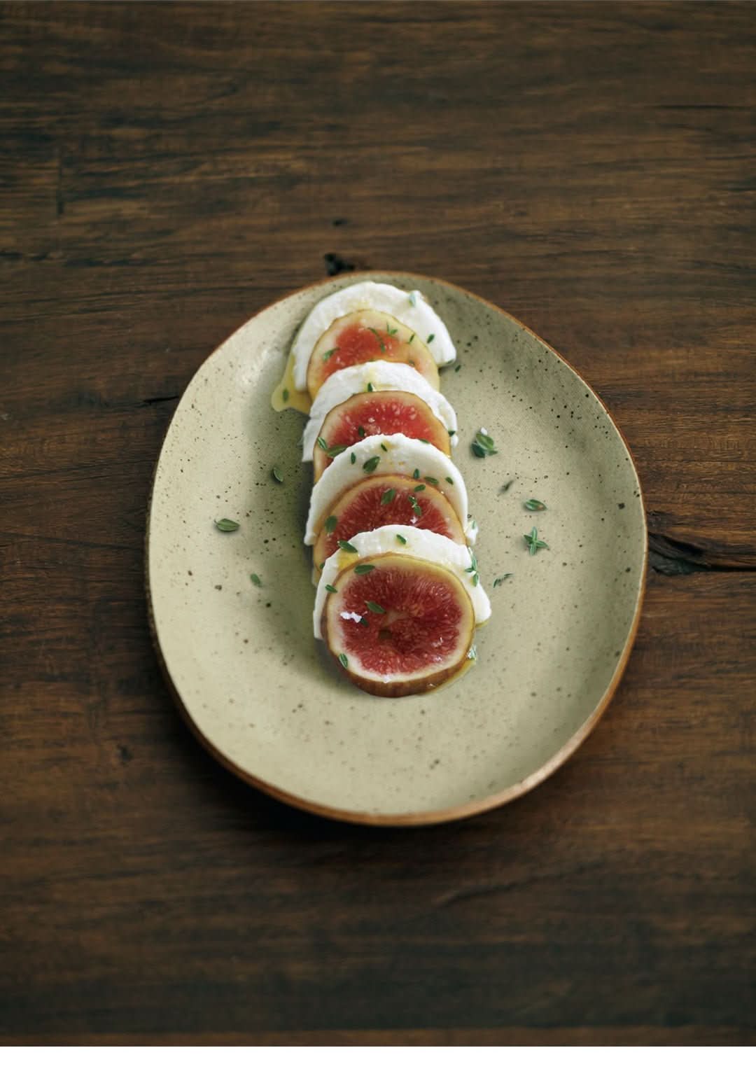 Handmade unglazed earthenware dinner plate with fig and mozzarella salad on rustic wood.