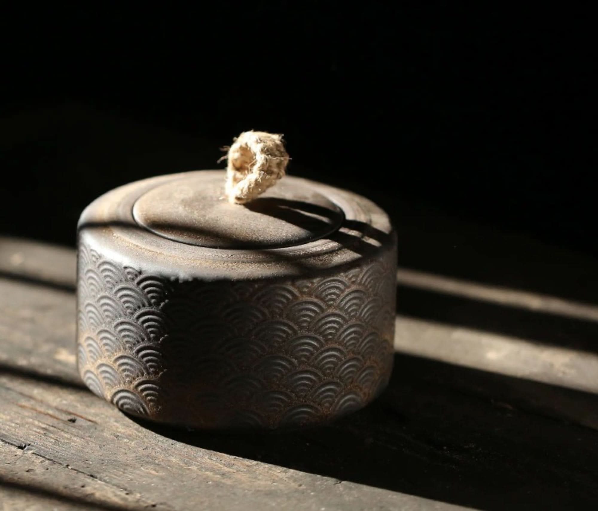 Dark patterned ceramic vintage kitchen canister with rope handle on wood.