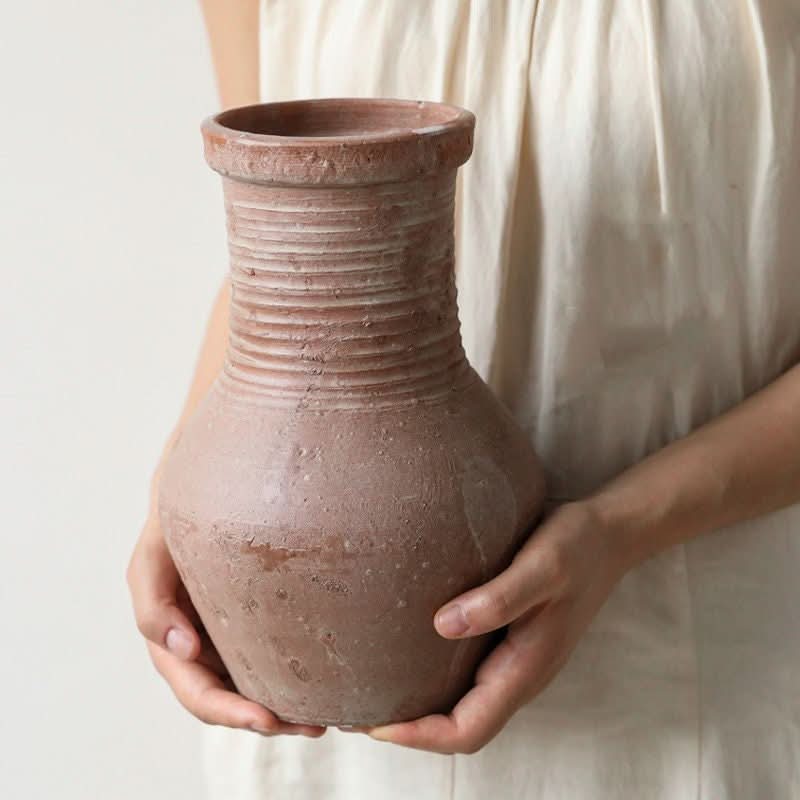 Vintage stoneware vase, red clay pot decoration with ribbed texture, held by hands.