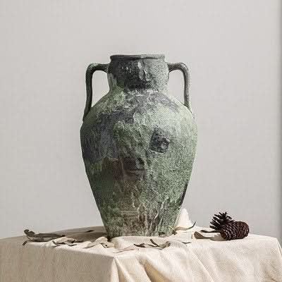 Wabi-Sabi Distressed Vase, textured gray tones, on a draped table with pinecone accent.