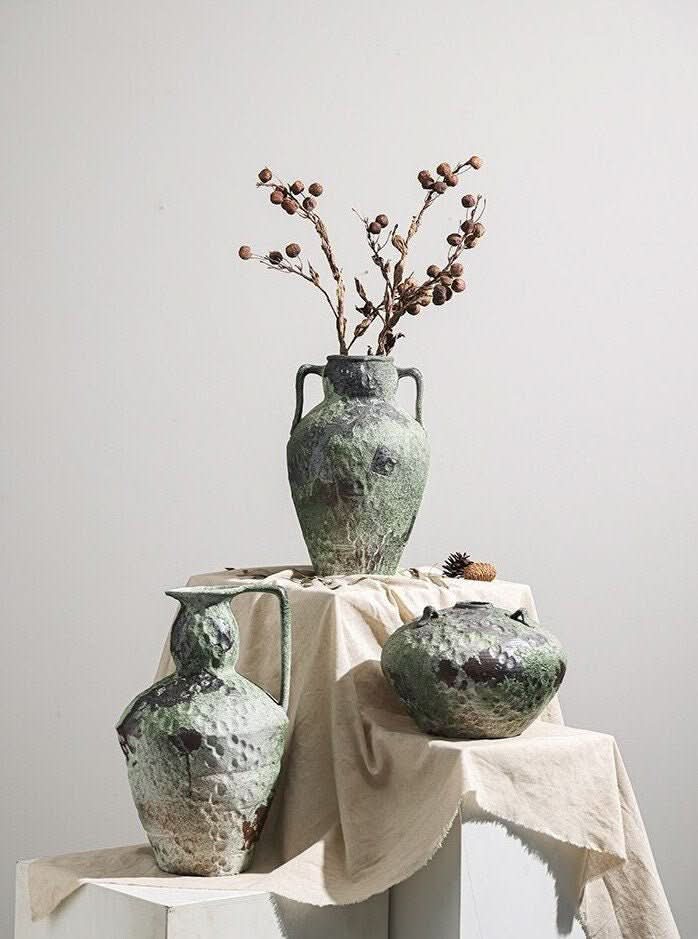 Wabi-Sabi distressed vases in muted green and gray tones, with dried branches, on a textured surface.