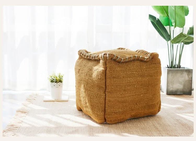 Wabi-sabi jute ottoman footstool with woven rope trim on a textured rug.