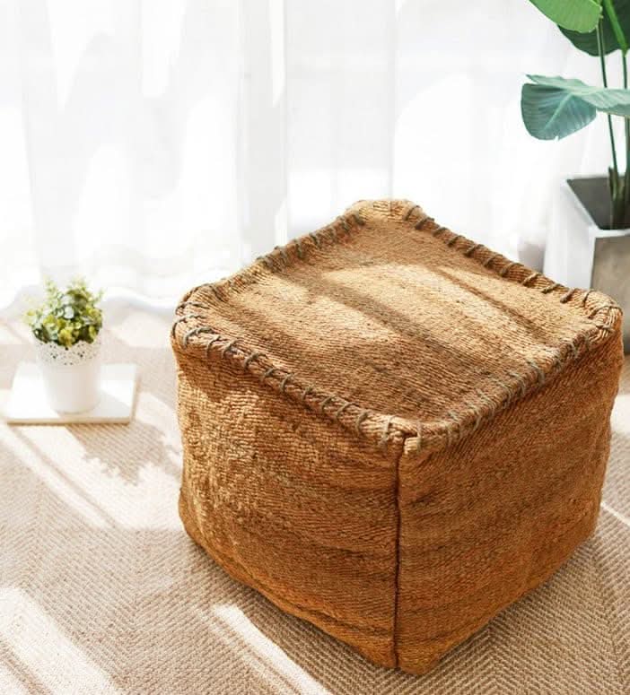 Wabi-sabi jute ottoman footstool, handmade brown textured pouf on woven rug with plants.