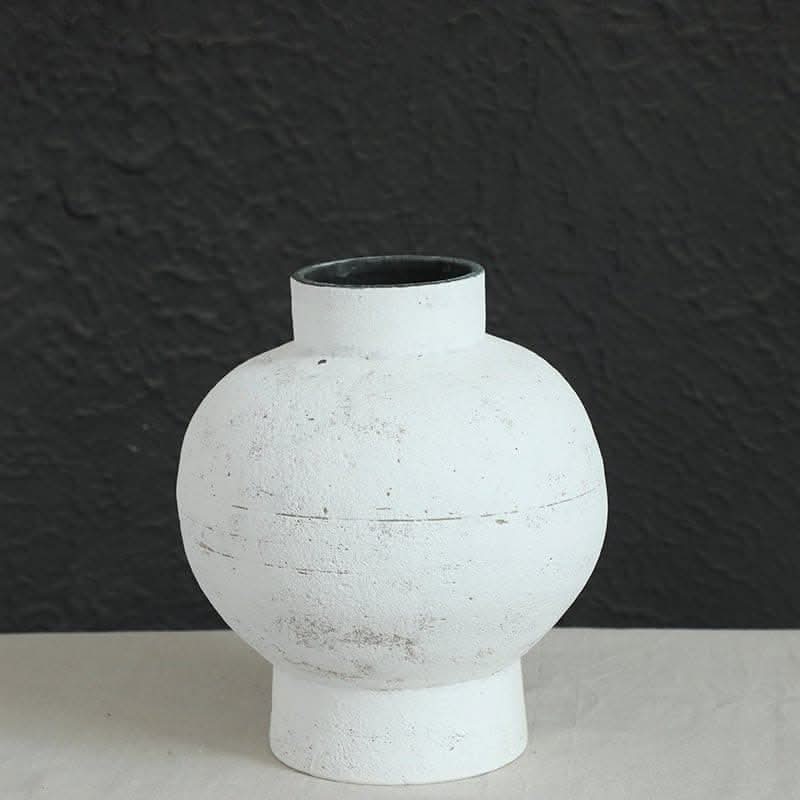 Wabi-sabi white clay pot, round with tight opening, on a neutral surface against a dark textured background.