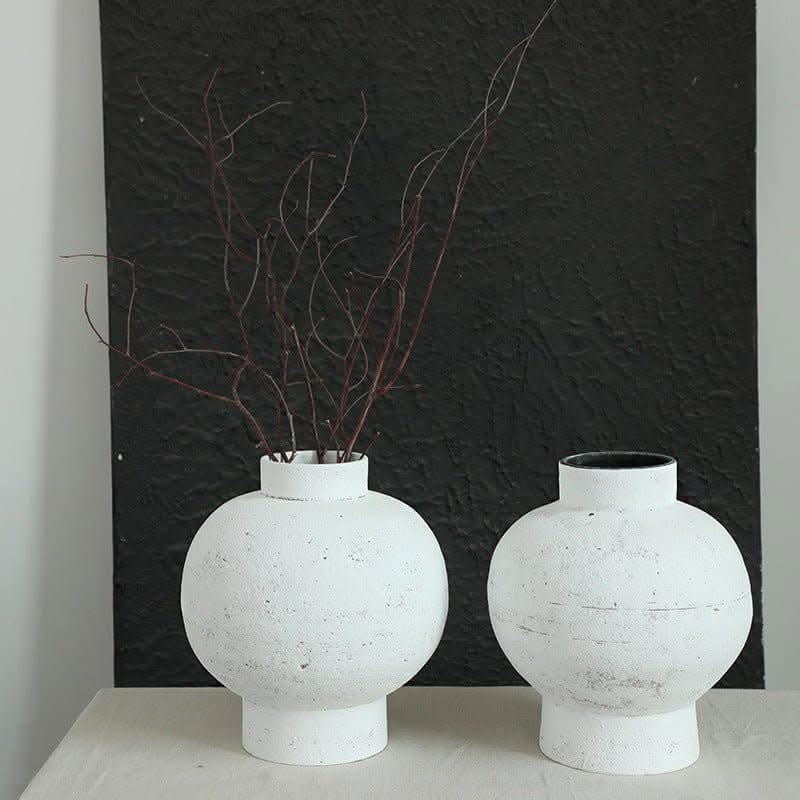 Wabi-sabi white clay pot, round with tight opening, holding dried branches on textured black background.