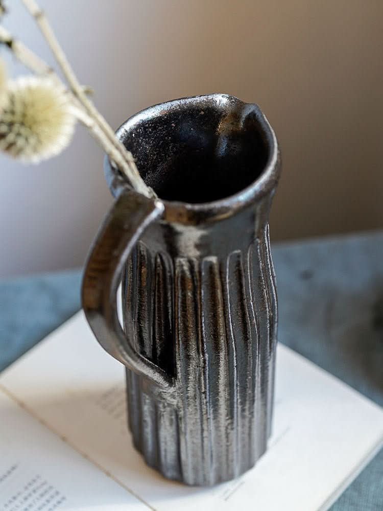 Black glaze cylindrical carved vase with handle, holding dried plant.