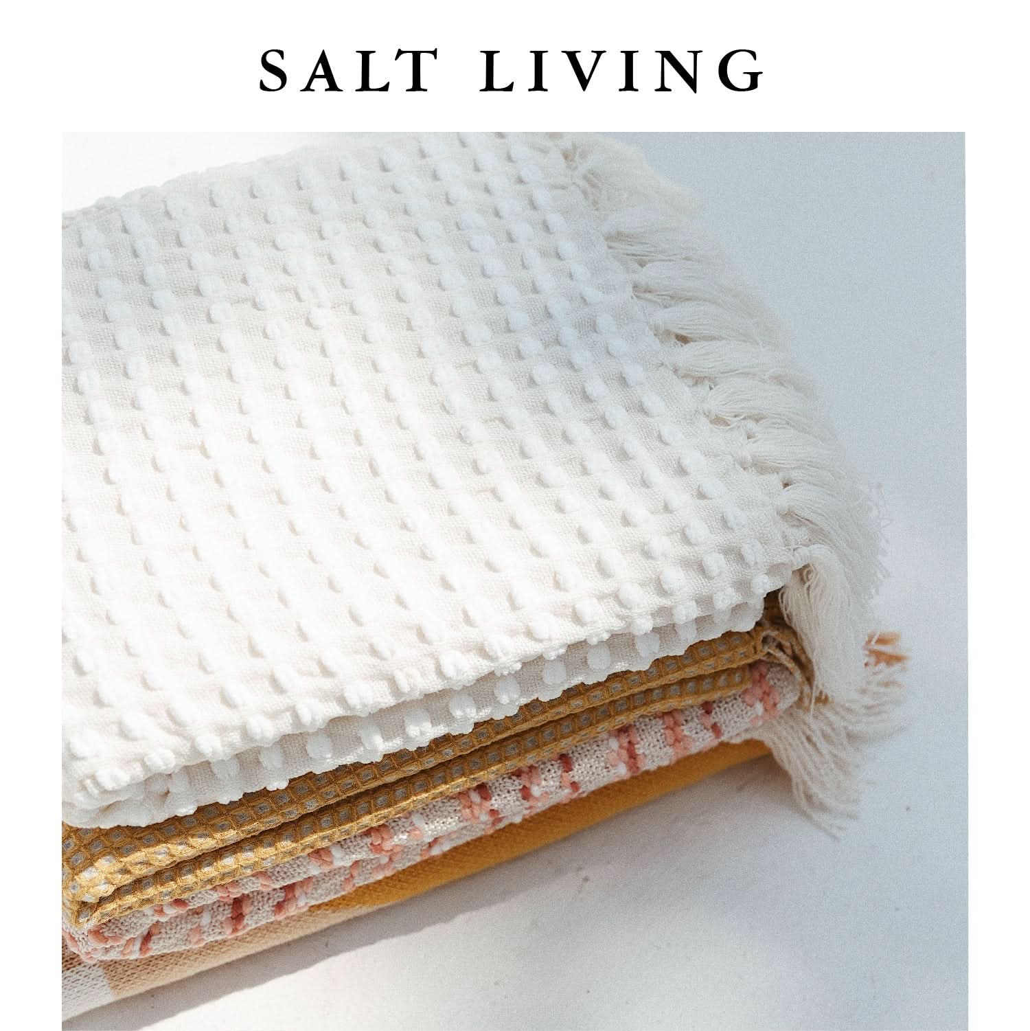 White chenille hand-loomed mud cloth blanket with tasseled edges, folded on white surface.