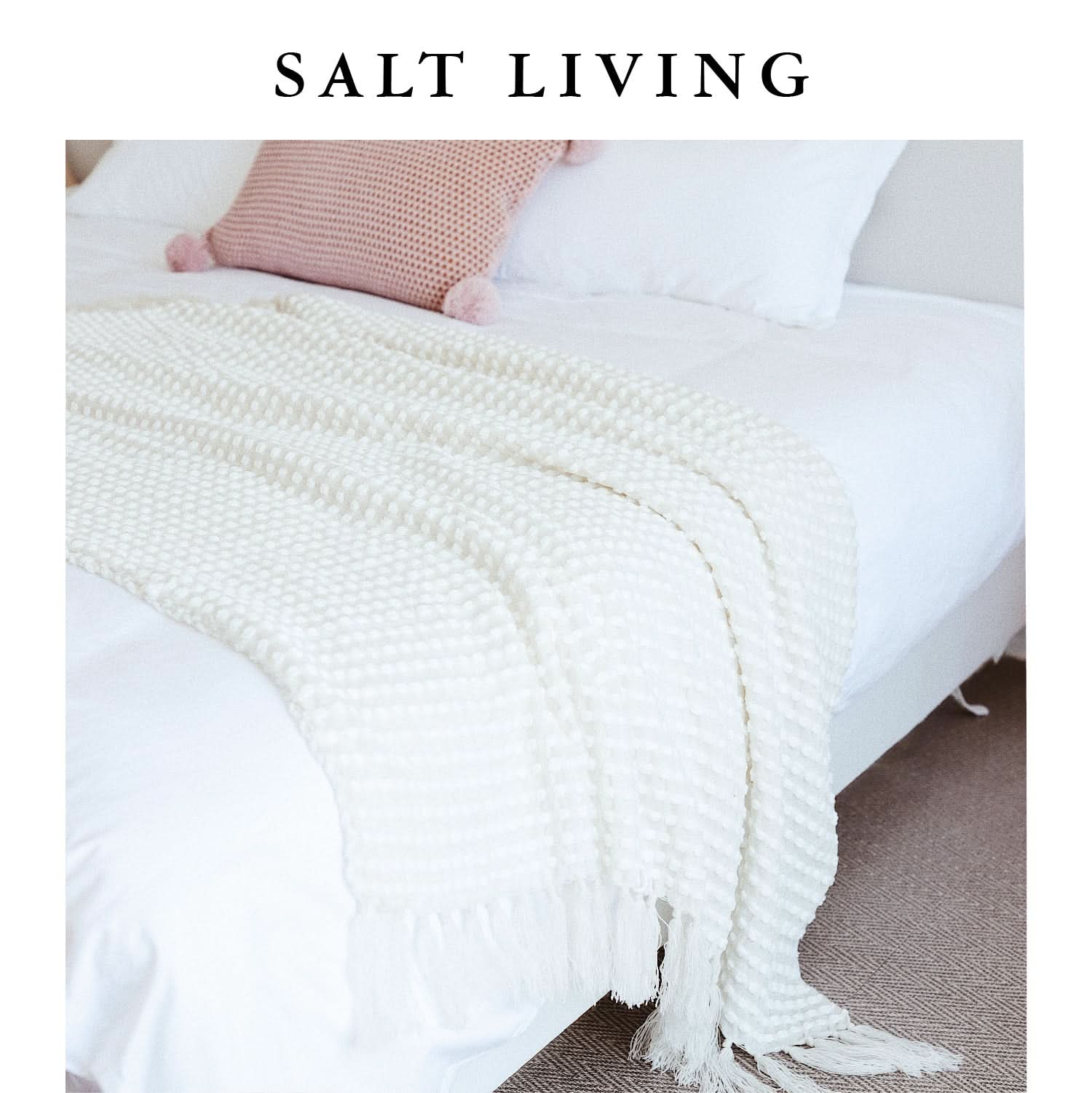 White chenille hand-loomed blanket with fringe, styled on a white bed with a pink accent pillow.