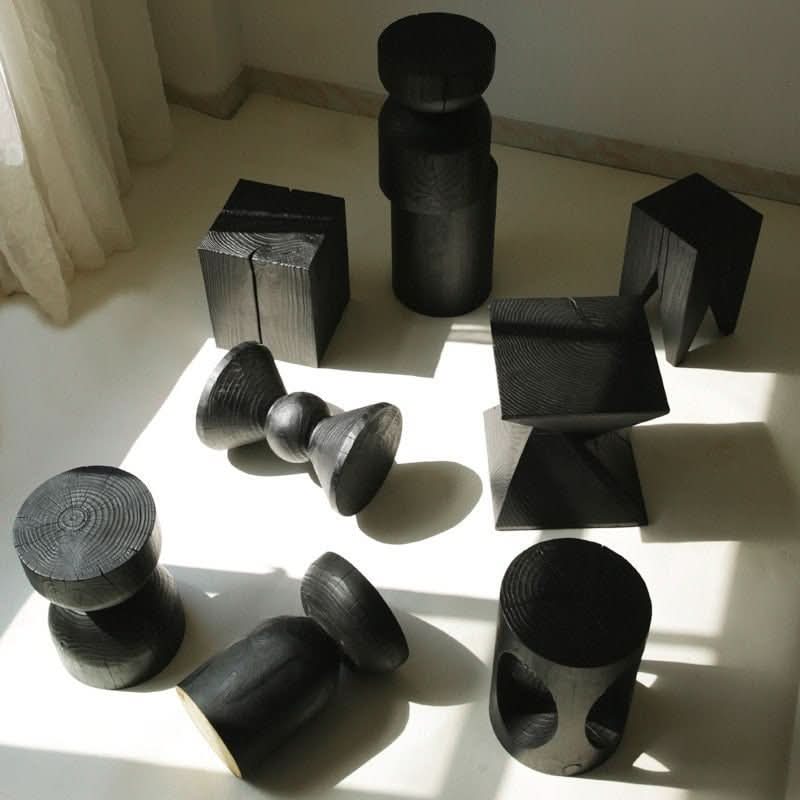 Various black wood stools in different shapes and sizes on a white floor.
