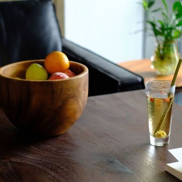 Acacia wooden bowl filled with fruit, next to a glass of drink on a dark wood table.